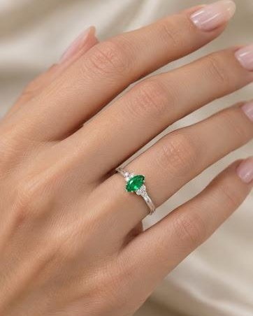 Mão feminina usando anel delicado com pedra verde navete e pontos de luz